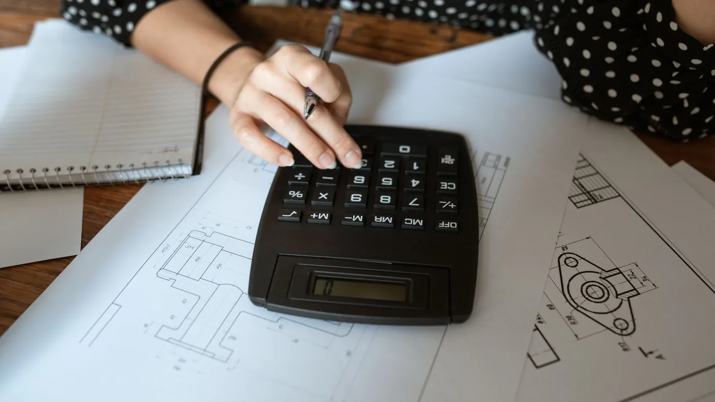 Hand using a calculator over printed technical drawings