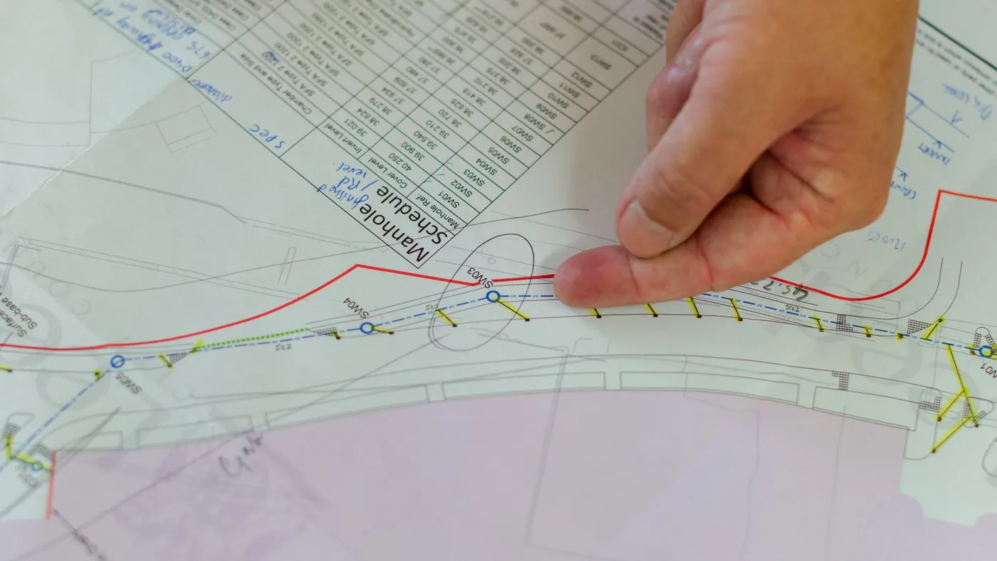 Hand pointing at a detail on a set of site drawings