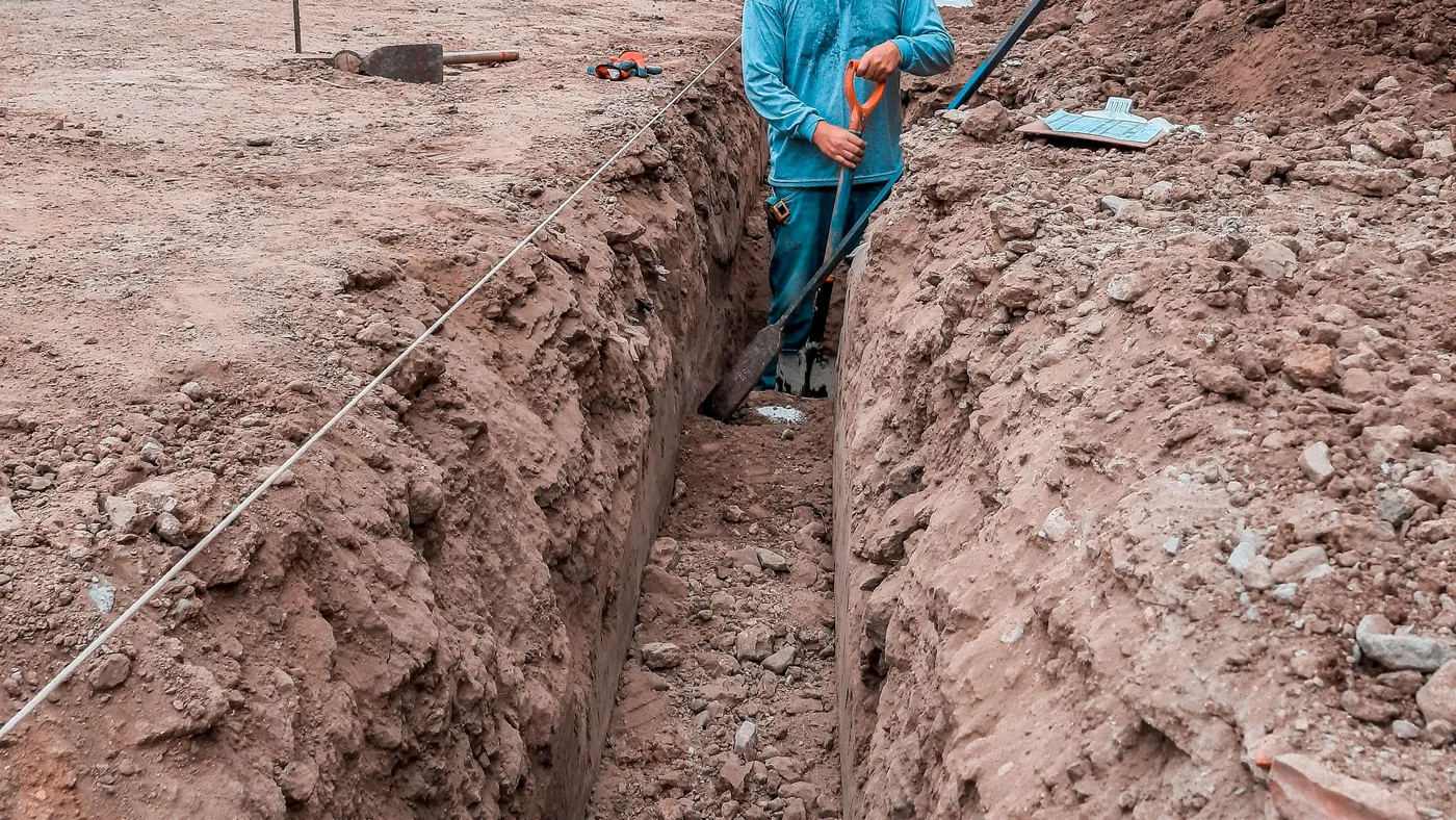 Worker in a deep excavated trench beside a row of buildings