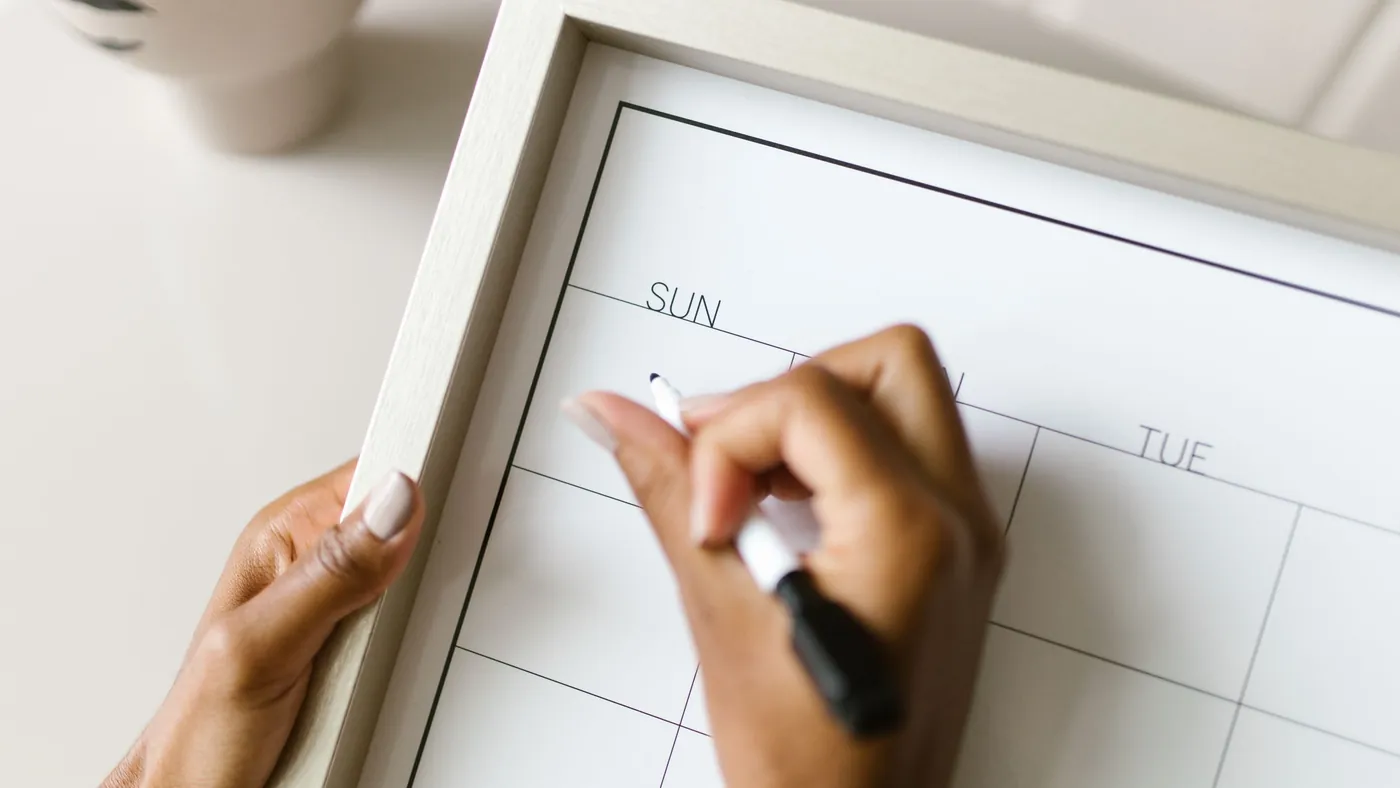 Hand writing on a wall planner calendar with a marker
